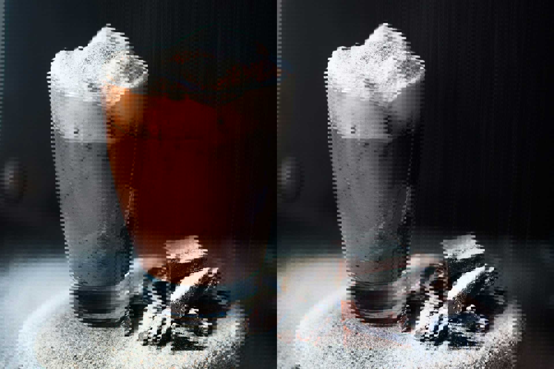 Et glas varm chokolade med skum og kakaodrys ved siden af chokoladestykker dækket af flormelis.