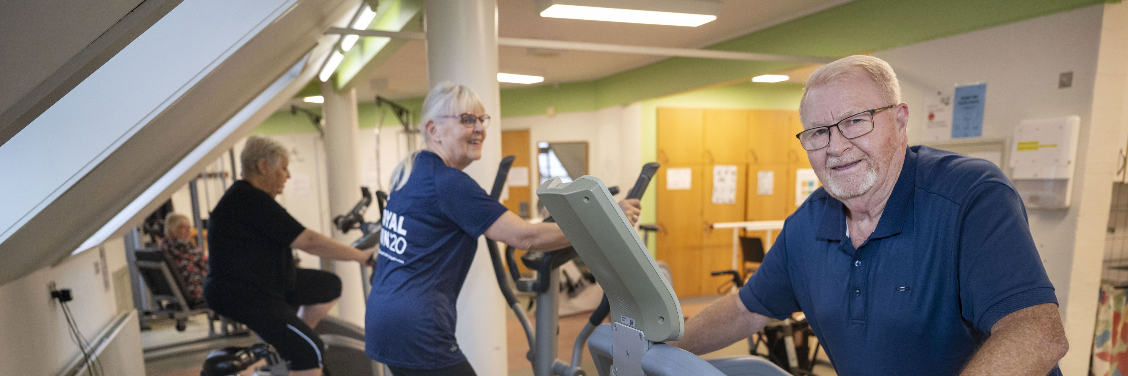 En ældre mand og to ældre kvinder træner på løbebånd, crosstrainer og motionscykel i træningslokale