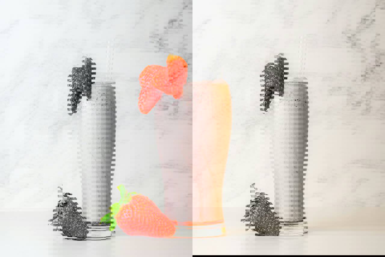 Et højt glas med jordbærmilkshake toppet med to sugerør og pyntet med friske jordbær, placeret på en lys baggrund.