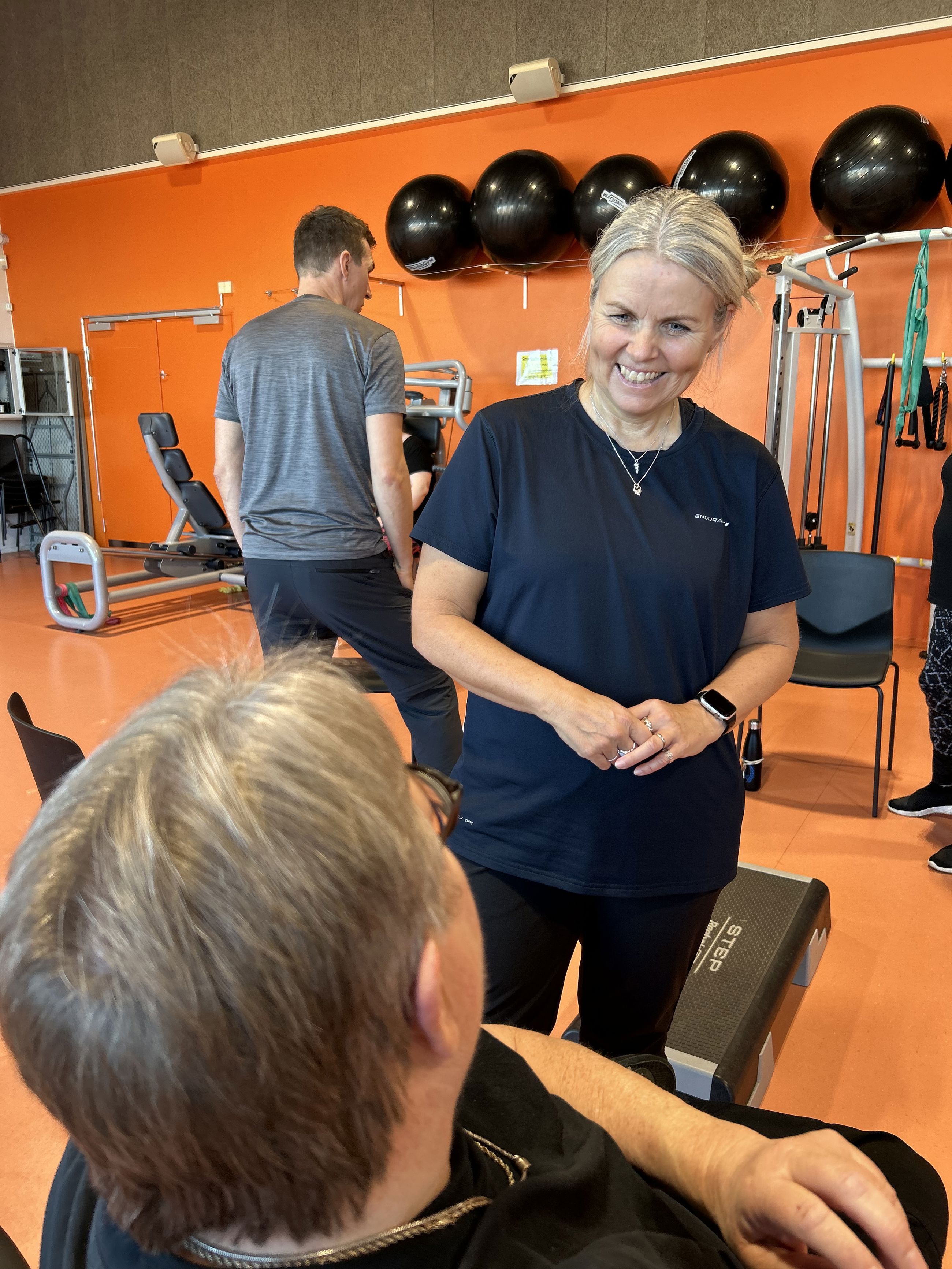 Stående kvinde taler med siddende i en træningssal