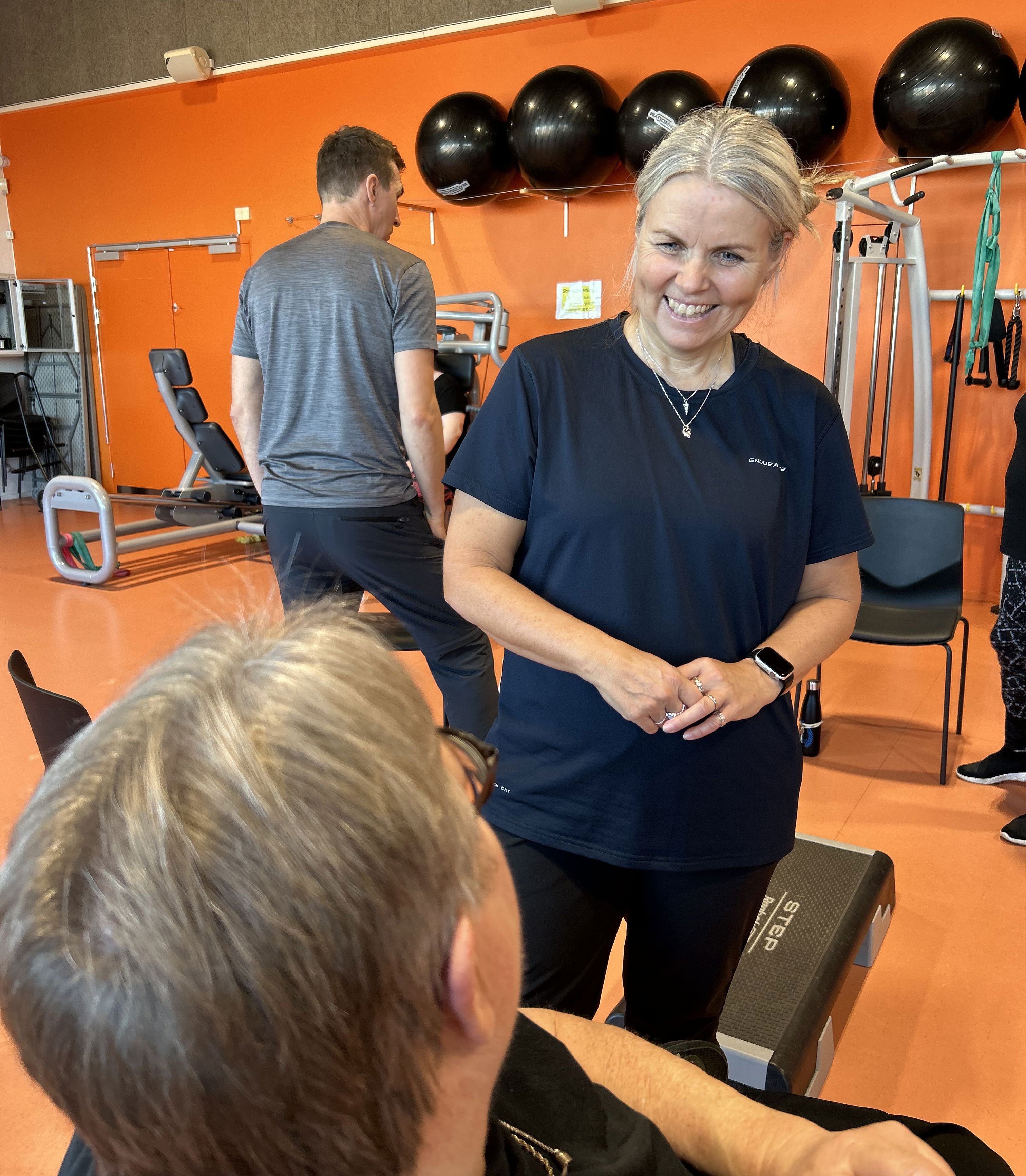 Stående kvinde taler med siddende i en træningssal