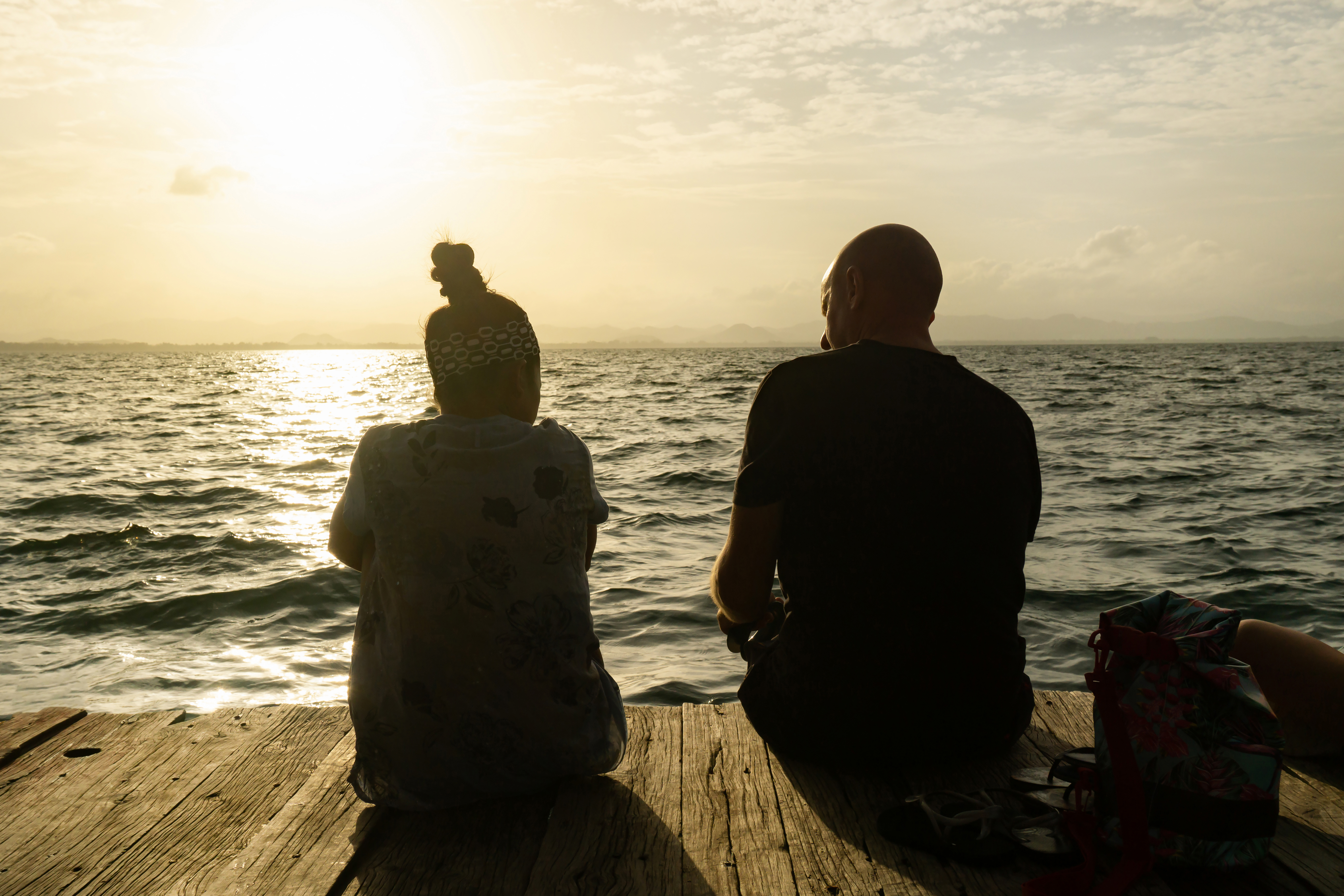 To personer sidder på badebro og ser solnedgang