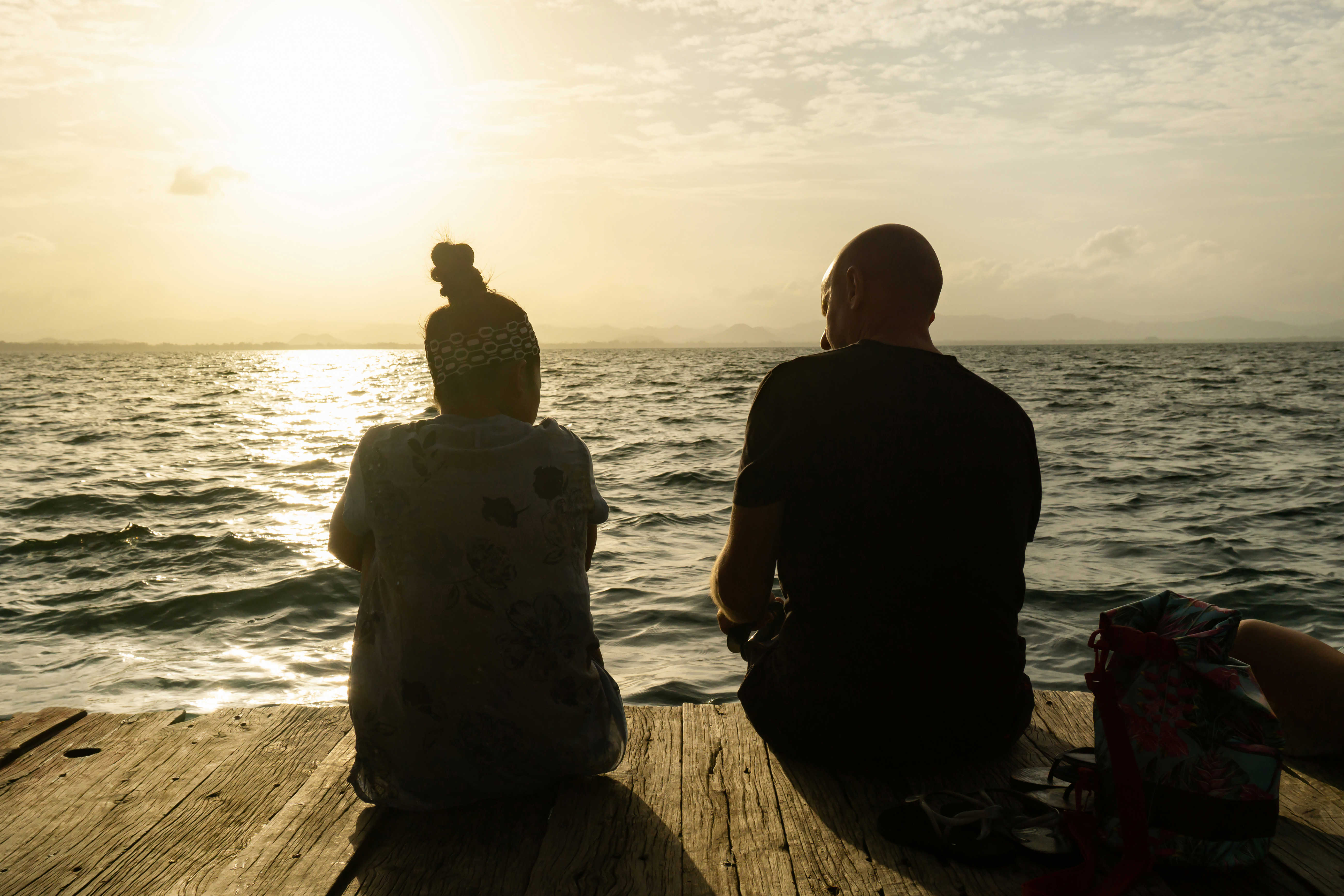 To personer sidder på badebro og ser solnedgang
